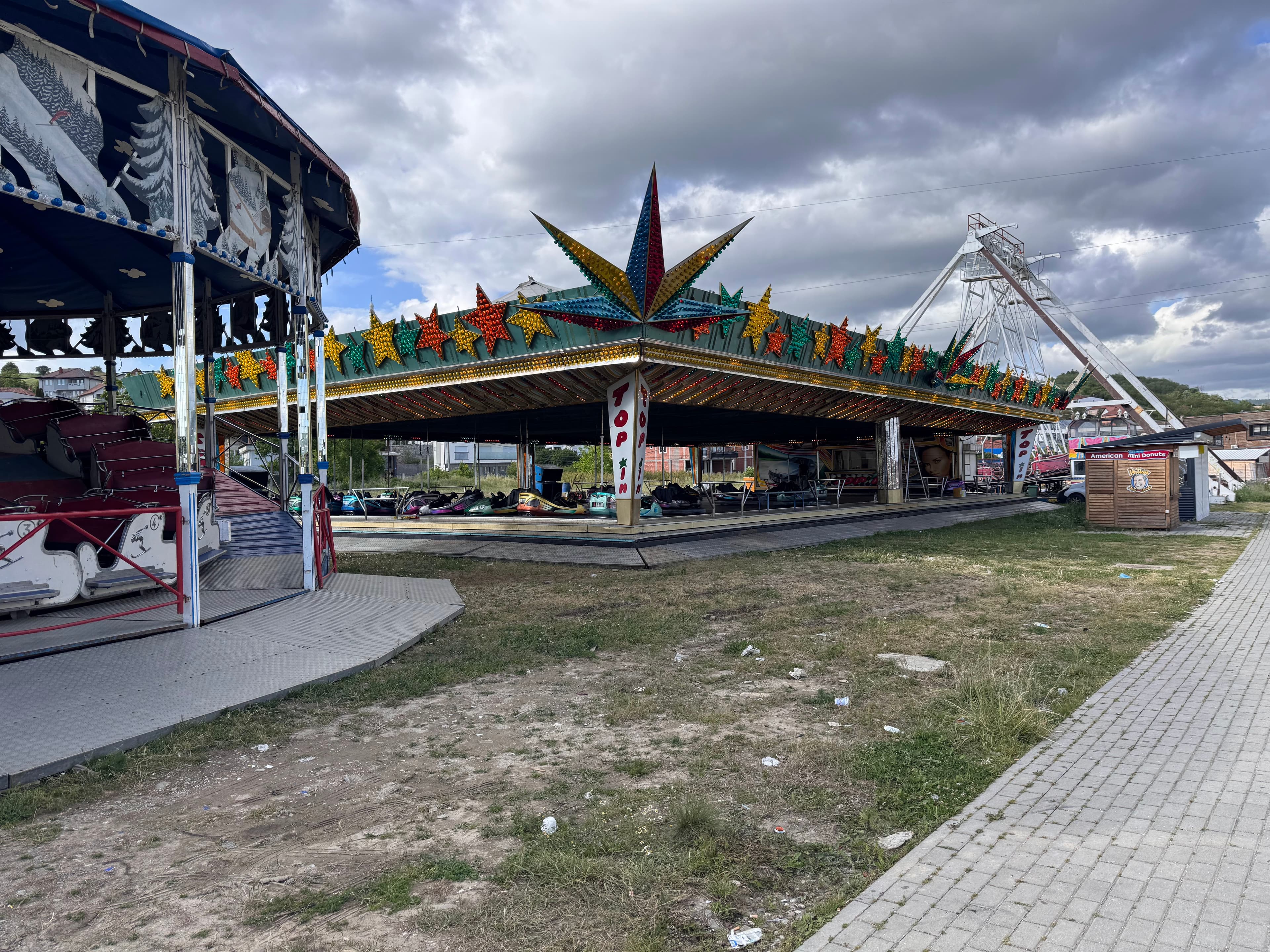 A fairground photo showing a bumper car ride branded 'TOP JIN', a covered ski-themed ride, and a partially visible white lattice tower structure in the background.